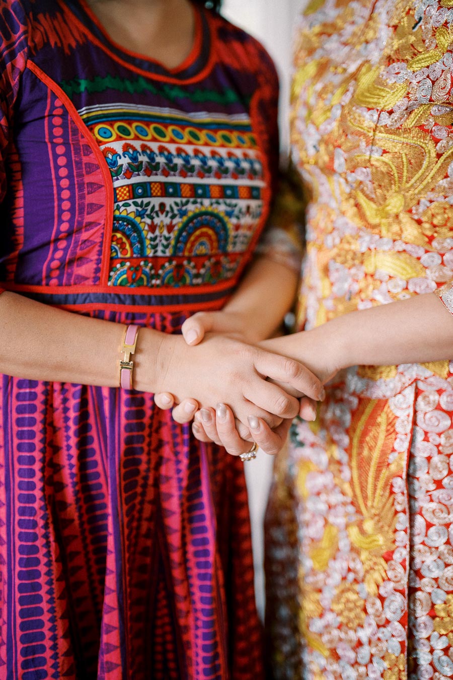 Two people holding hands, wearing vibrant, intricate traditional clothing featuring colorful patterns and embroidery.