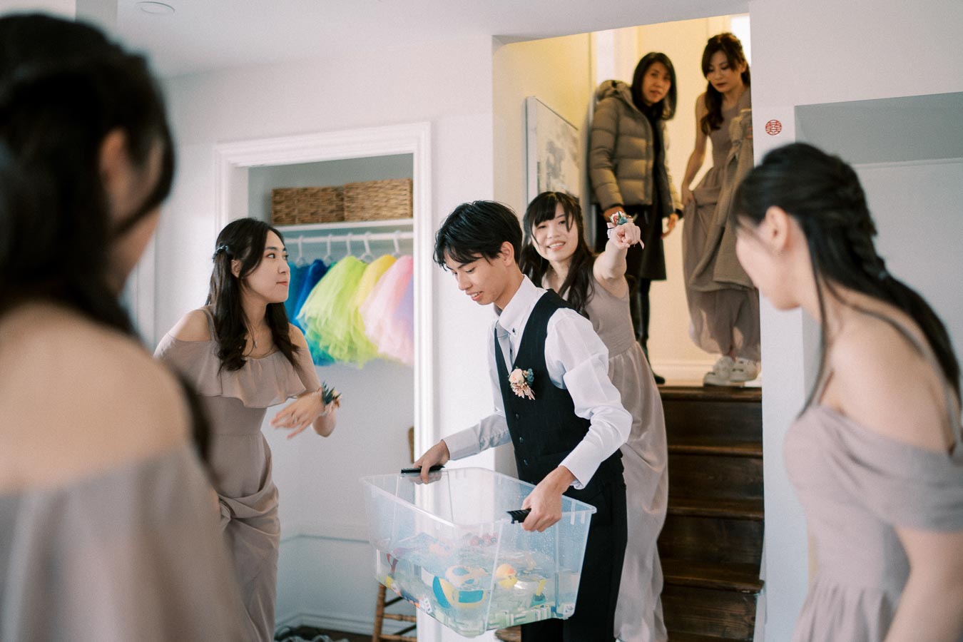 Group of young adults in formal attire enjoying a lighthearted moment during a gathering indoors, with colorful fabrics hanging in the background.