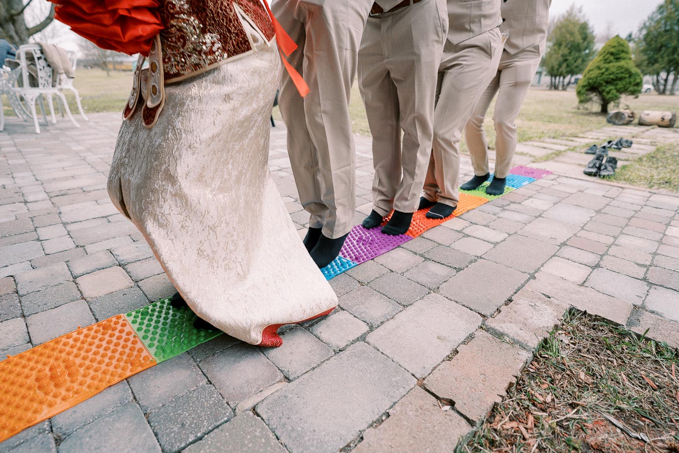 Guests at a wedding participate in a traditional outdoor walking ceremony, stepping barefoot on a colorful textured mat, showcasing cultural attire and celebration.