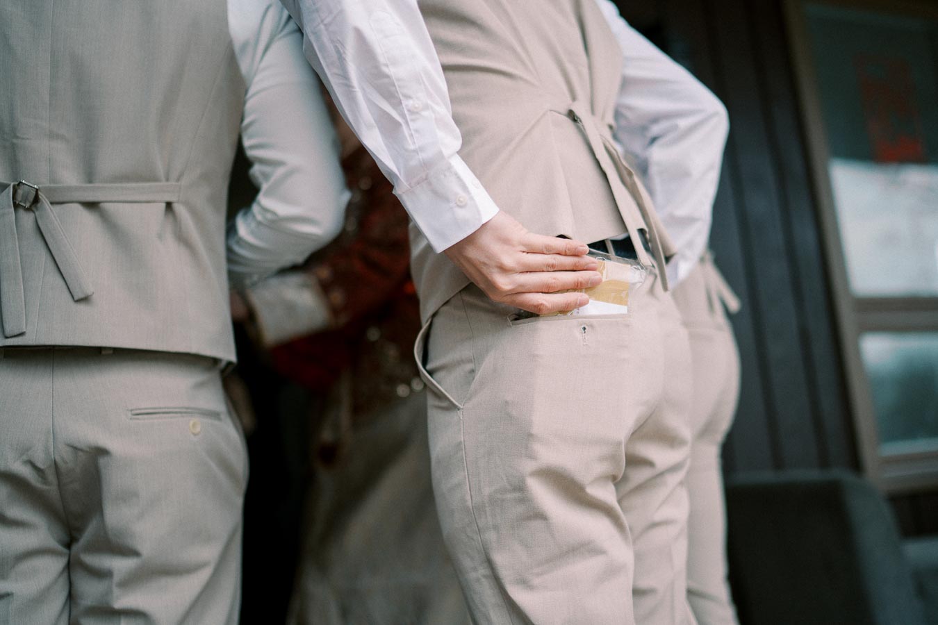 A group of people in beige suits standing together, one person holding a drink pouch and placing it in their back pocket, seen from behind.