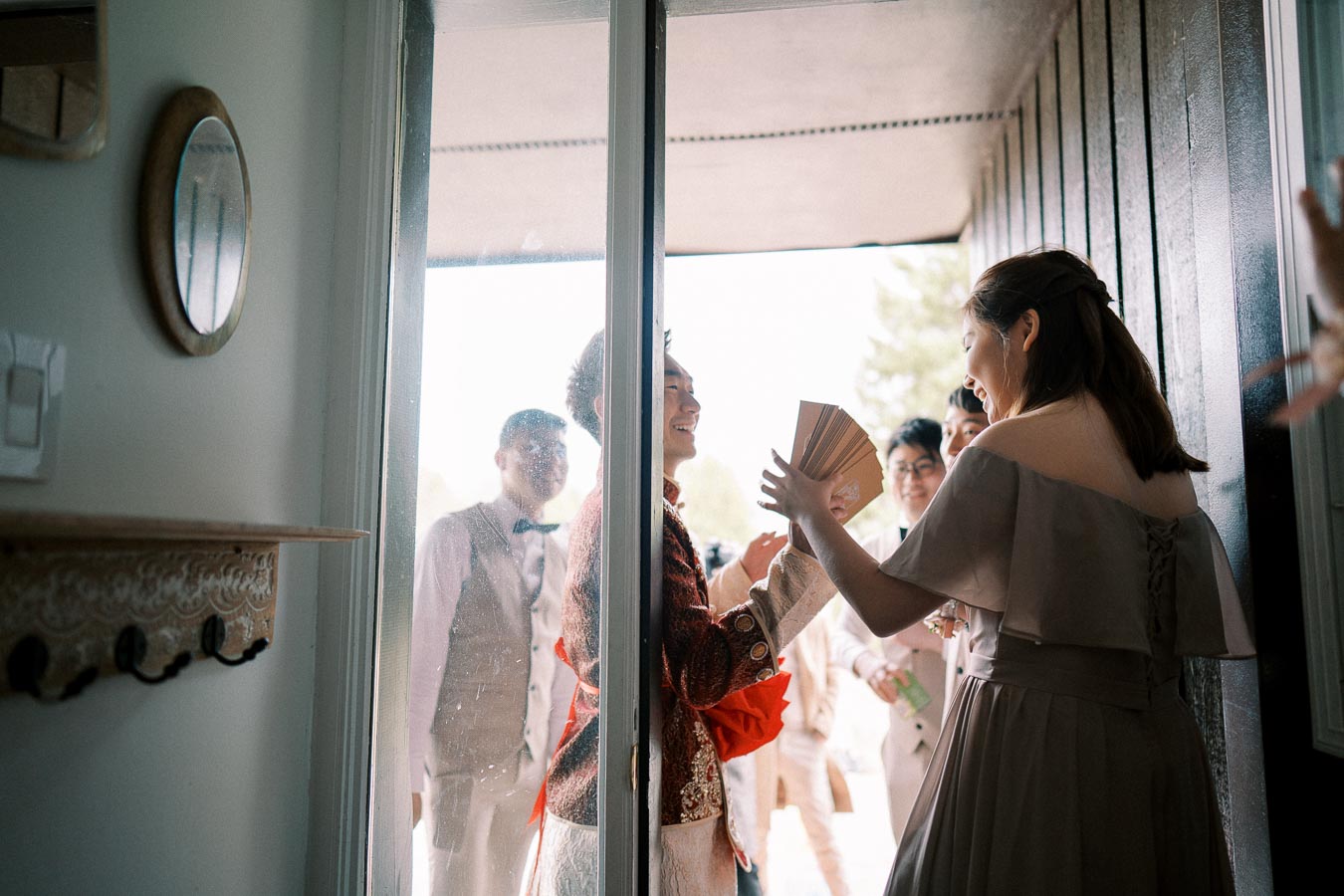 A joyful wedding gathering with a bride and groom sharing a moment through a glass door, surrounded by wedding guests in elegant attire, capturing a candid celebration scene.