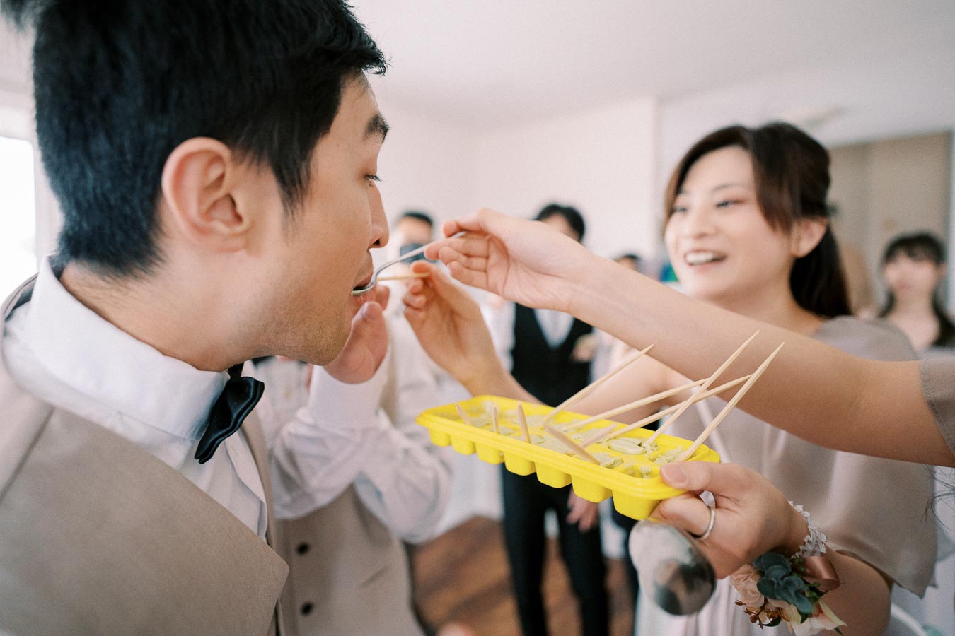 Group of people enjoying a fun ice cube game at a gathering, with one person playfully feeding another using a toothpick from a yellow ice cube tray.