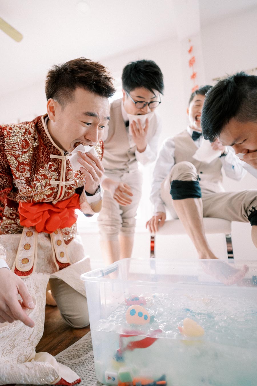 Group of men in traditional and modern attire participating in a playful game involving ice water and toys, indoors.