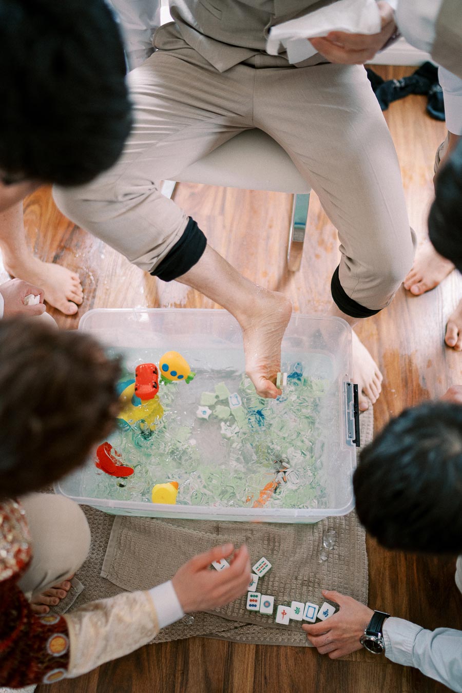 Fun bridal shower game with man using foot to pick Mahjong tiles from a bin of ice water and toy fish surrounded by people.
