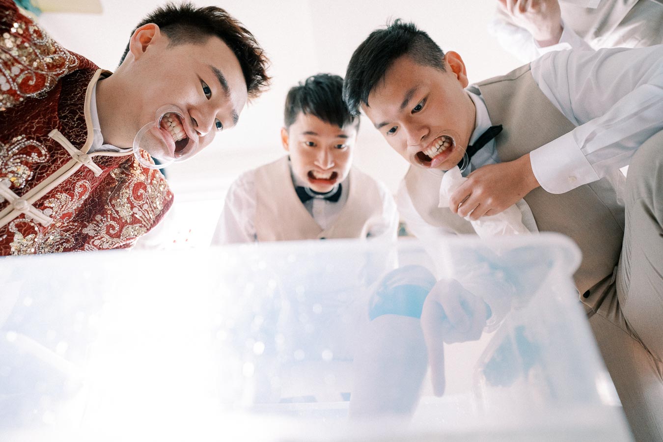 Playful wedding challenge with groomsmen in traditional attire and bow ties using mouthguards, expressing excitement and amusement.