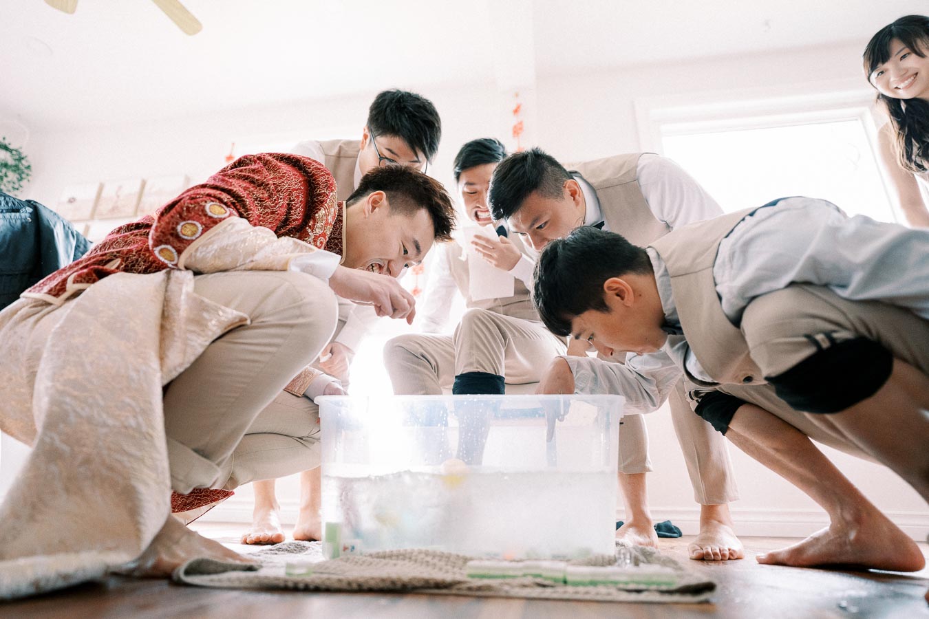 A group of people enthusiastically participate in a fun game or activity, leaning over a tub filled with water, inside a bright room.