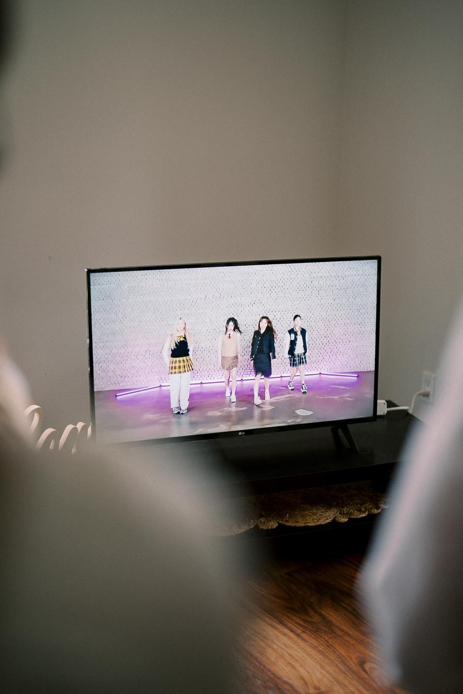 A TV screen displaying a dance performance, featuring four individuals in colorful outfits, set against a patterned backdrop with purple lighting.
