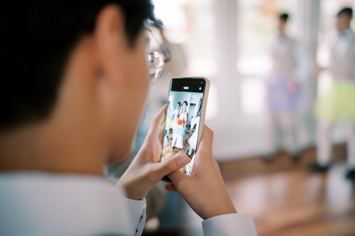 Person taking a photo with a smartphone, capturing a group in a bright, indoor setting.