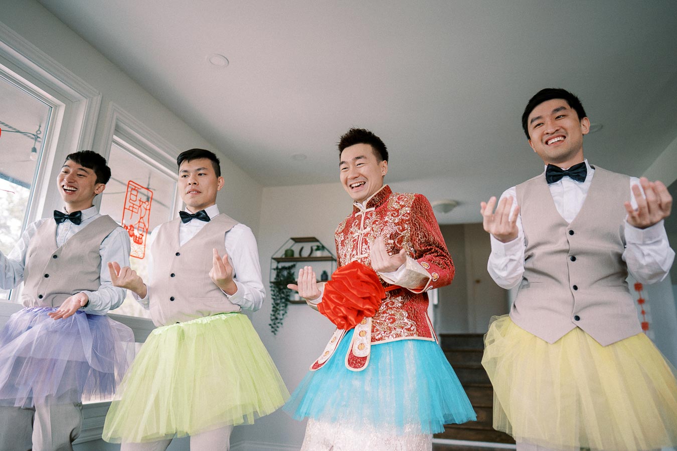 Four men wearing colorful tutus and vests, having fun indoors during a festive celebration, with cheerful expressions.