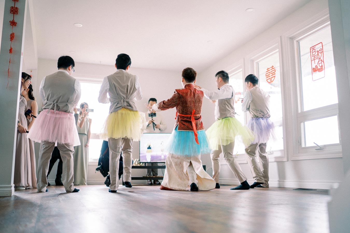 Group of people at a wedding celebration, featuring groomsmen in colorful tutus and traditional decor, captured in a bright, festive atmosphere.