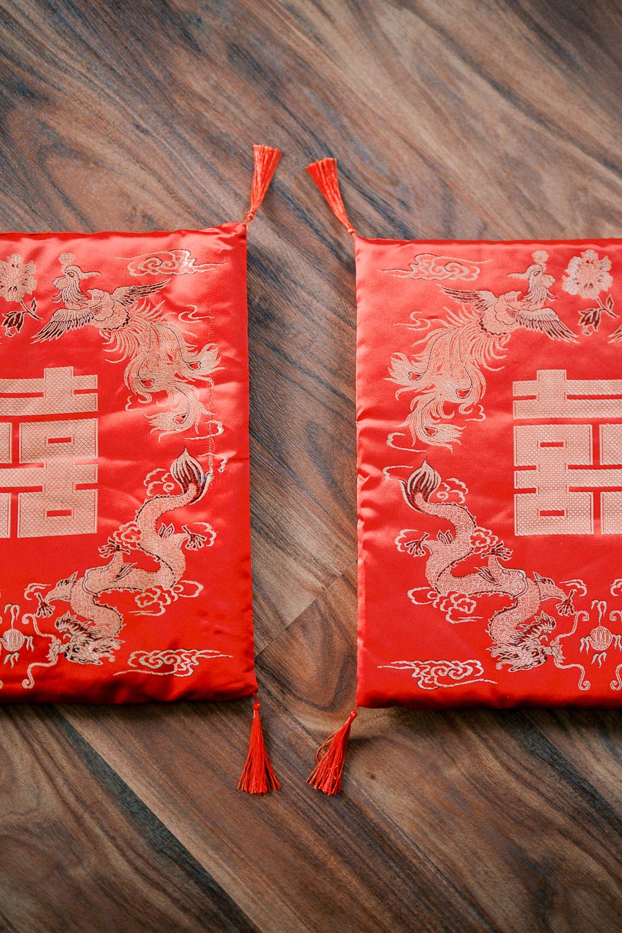 Two ornate red silk pillows with intricate embroidery featuring traditional Chinese motifs, including dragons and phoenixes, placed on a wooden floor. Perfect for cultural decor or themed events.