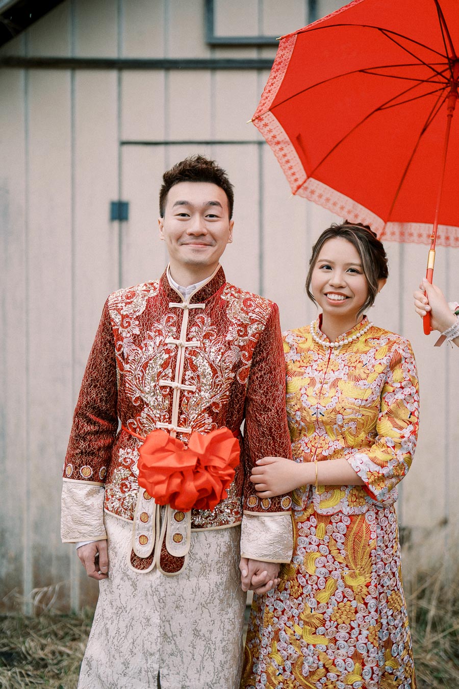 Young couple in traditional Chinese wedding attire, posing with a red umbrella.