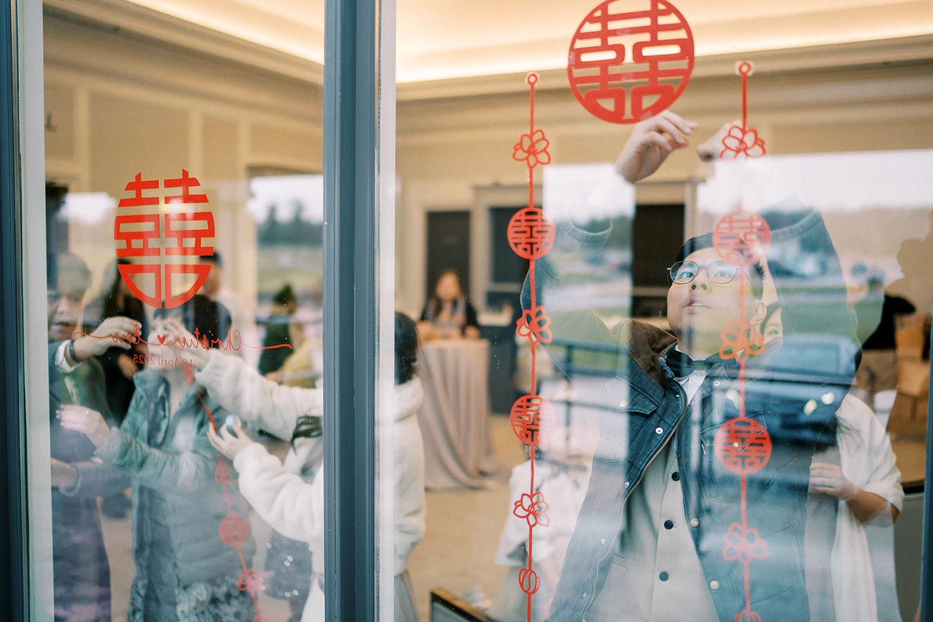 A person decorates a glass window with traditional Chinese red symbols for a celebration indoors.
