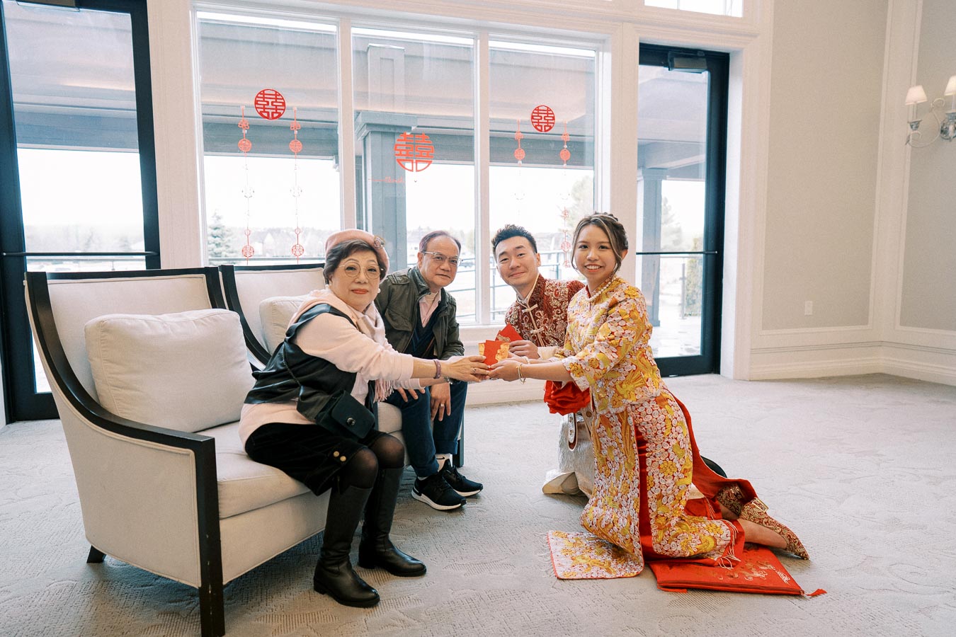 Asian family celebrating a traditional ceremony indoors, exchanging red envelopes, with festive decorations on the windows highlighting a cultural gathering.