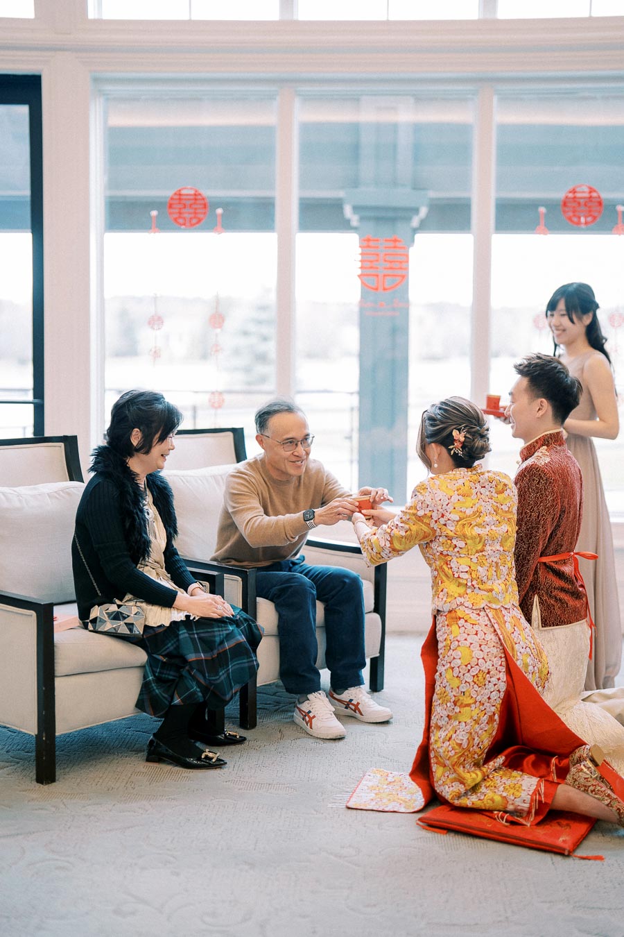 Traditional Chinese tea ceremony with couple in vibrant attire serving tea to seated family members in a beautifully decorated room.