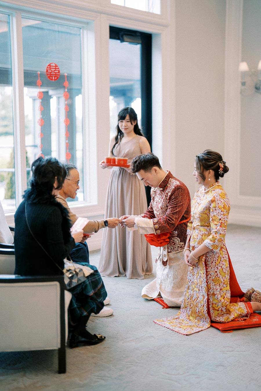 Traditional Chinese wedding tea ceremony with a bride and groom in ornate outfits kneeling before family, performing a cultural ritual of serving tea.