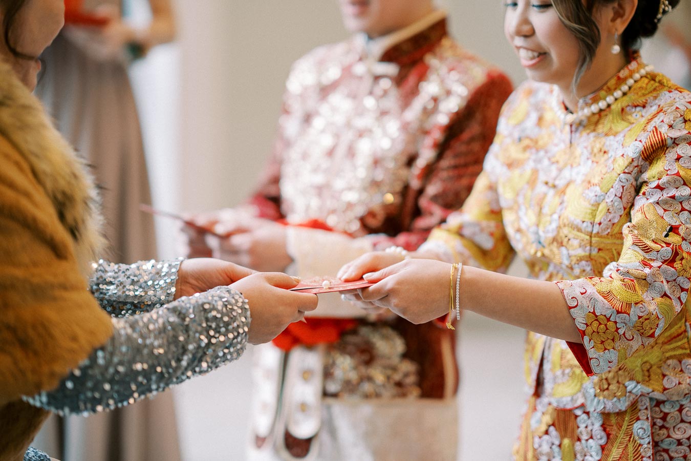 Ceremonial exchange of red envelopes at a traditional celebration, featuring individuals in ornate, embroidered attire symbolizing cultural heritage and prosperity.