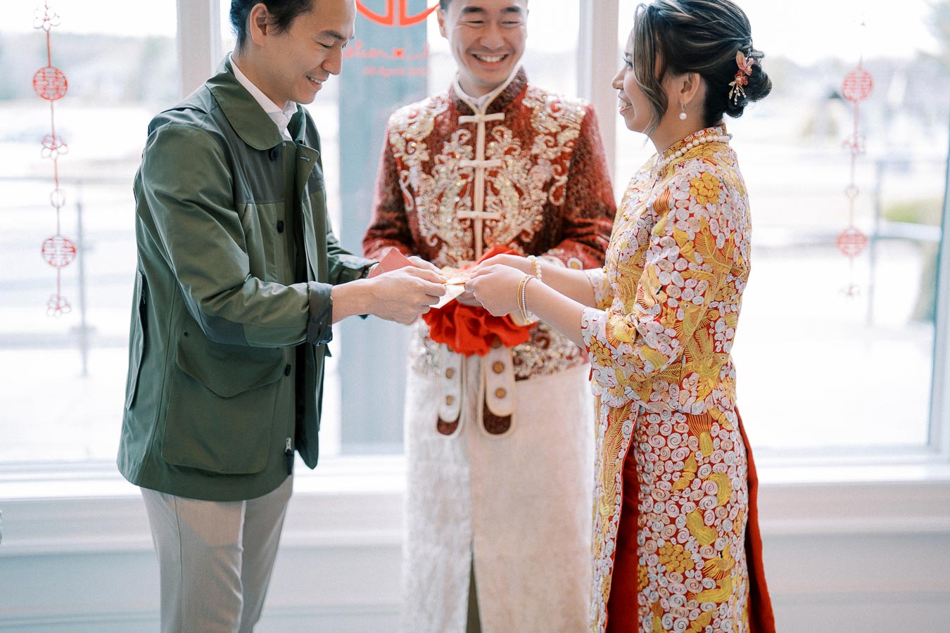 A couple exchanging wedding gifts during a traditional Asian ceremony, with intricate red and gold embroidered outfits, highlighting cultural heritage and celebration.