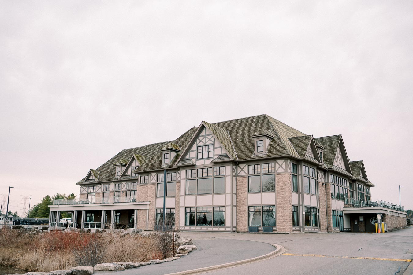 Exterior of a large, modern Tudor-style building with multiple gables, featuring large windows and a spacious driveway in the foreground.