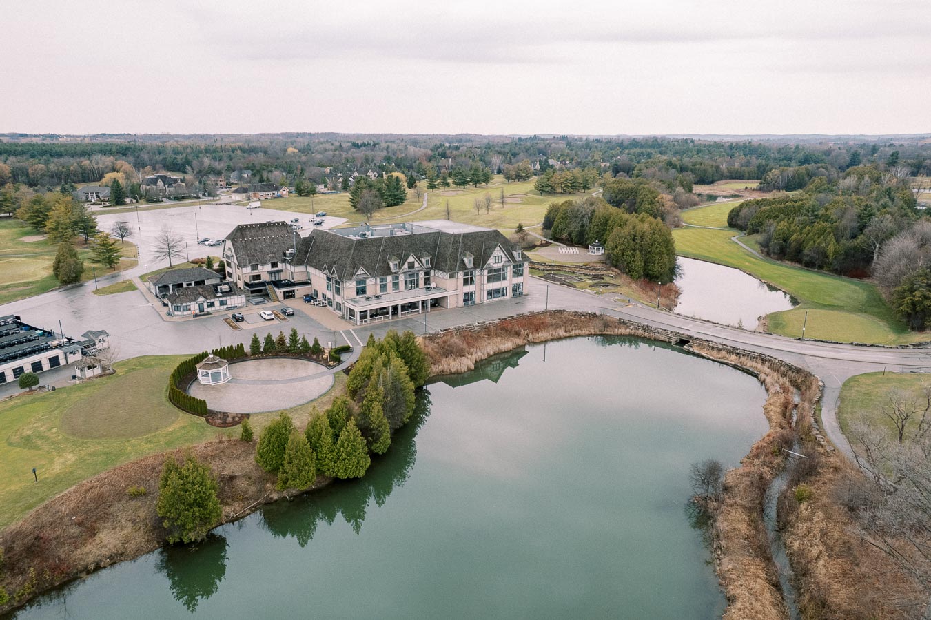 Aerial view of a large lakeside resort surrounded by lush greenery and golf courses, featuring a complex of buildings with pitched roofs and a scenic pond in the foreground.