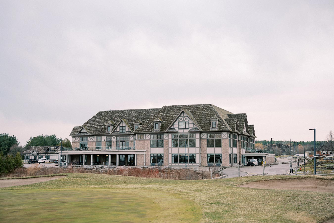 Tudor-style building with large windows surrounded by greenery and a cloudy sky.