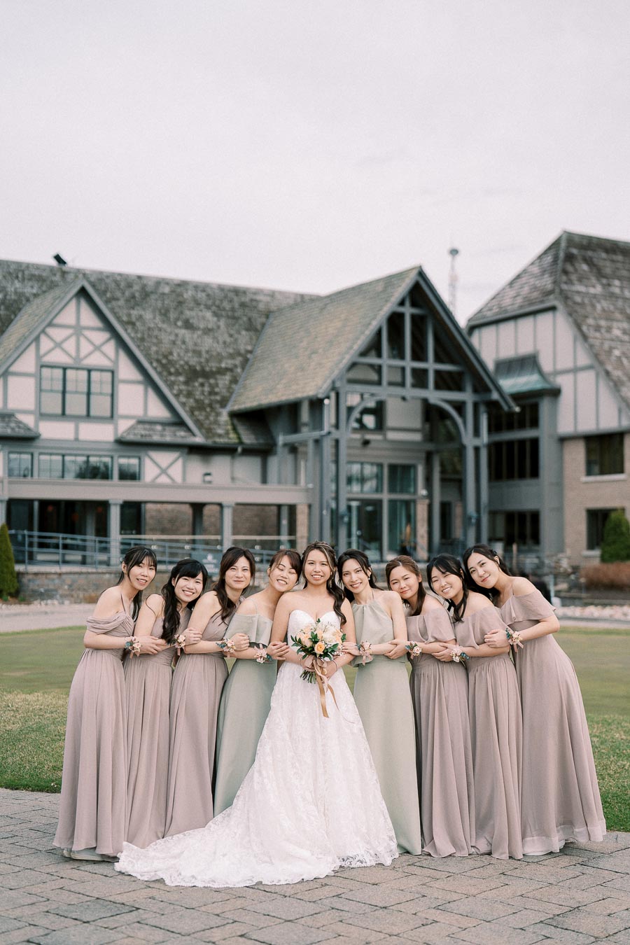 Bride and bridesmaids posing in matching dresses outside a Tudor-style building on a wedding day.
