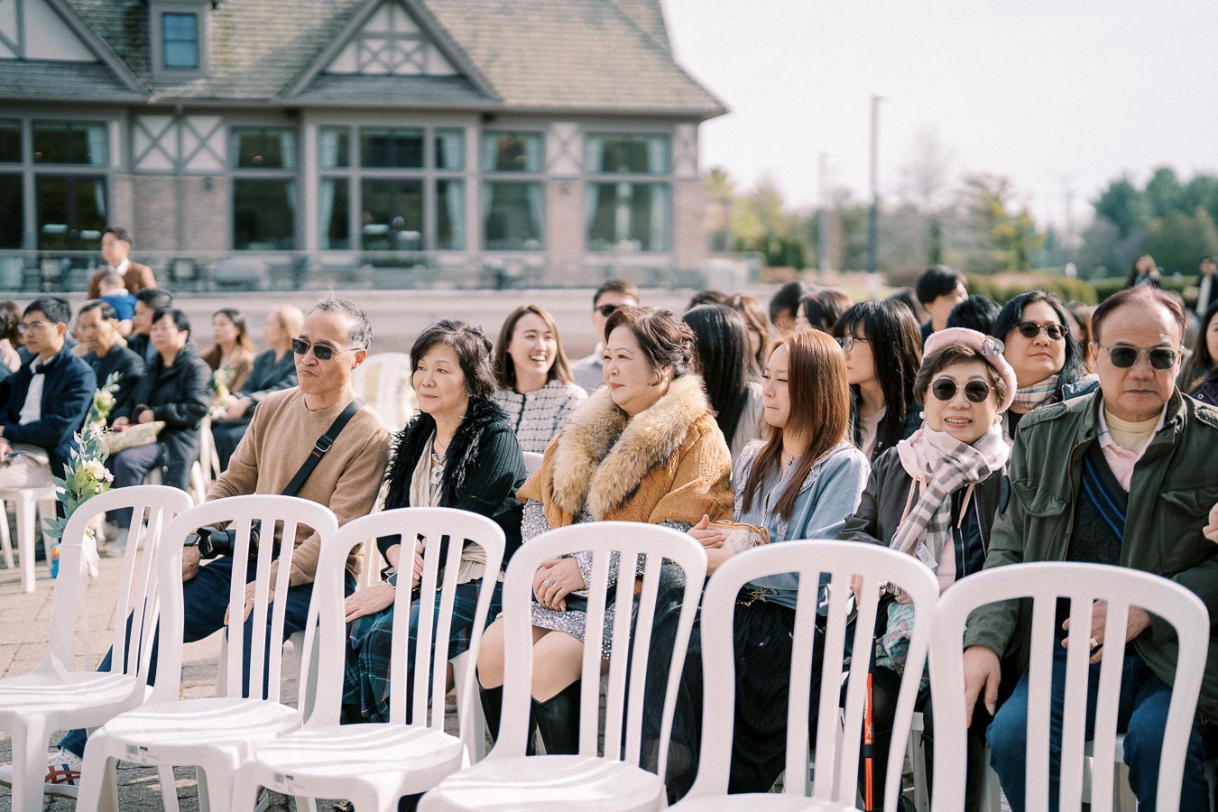 A group of people seated outdoors at a formal event, wearing winter clothing.