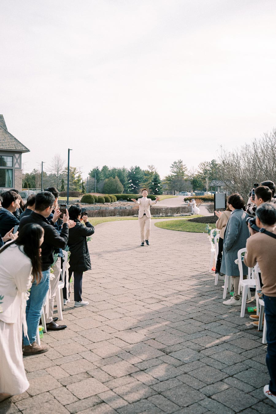 Wedding ceremony with a person joyfully tossing flower petals surrounded by a crowd of guests, set in an outdoor venue with a picturesque garden background.