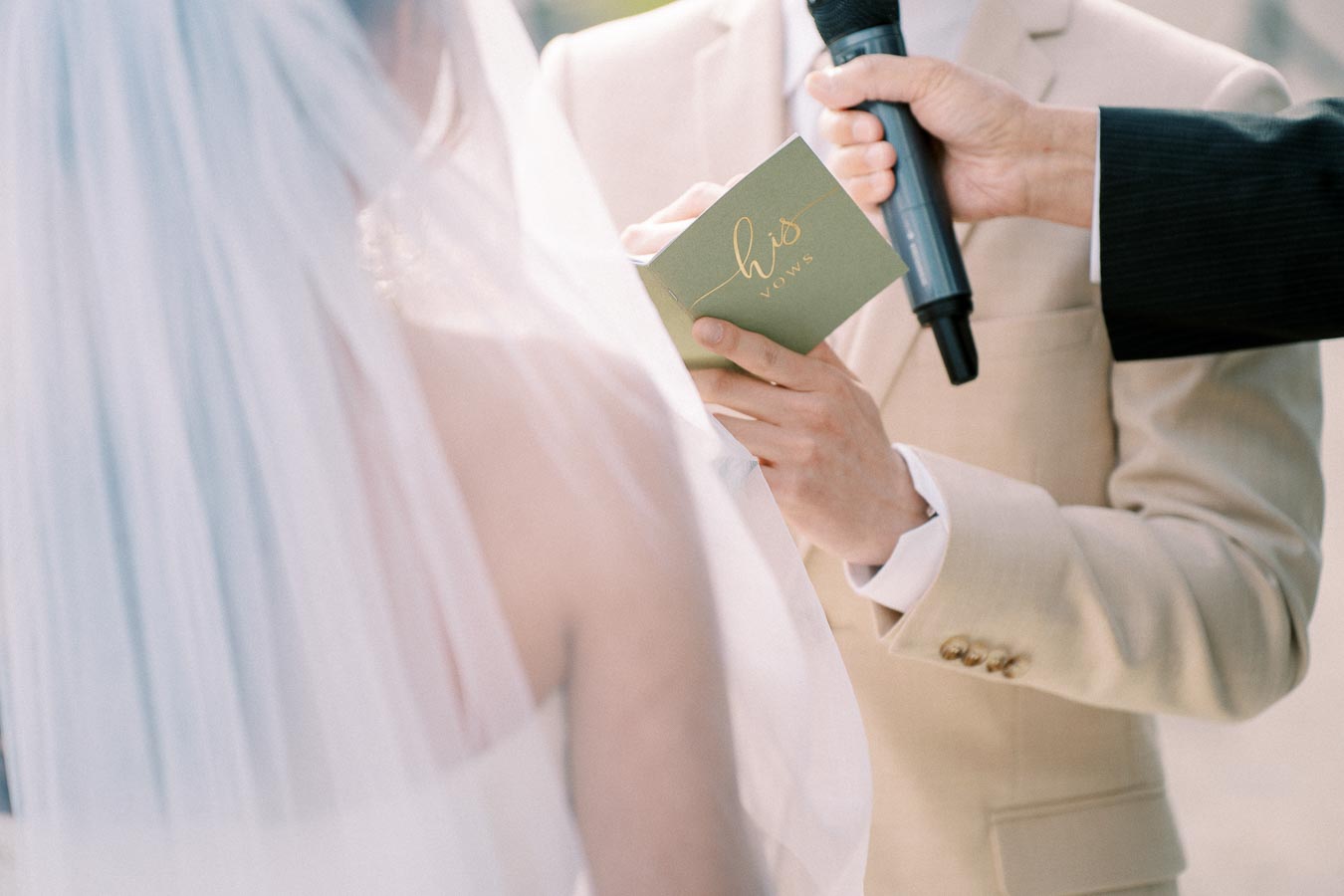 Bride and groom exchanging vows during a wedding ceremony, with the groom holding a microphone and a card titled his vows.