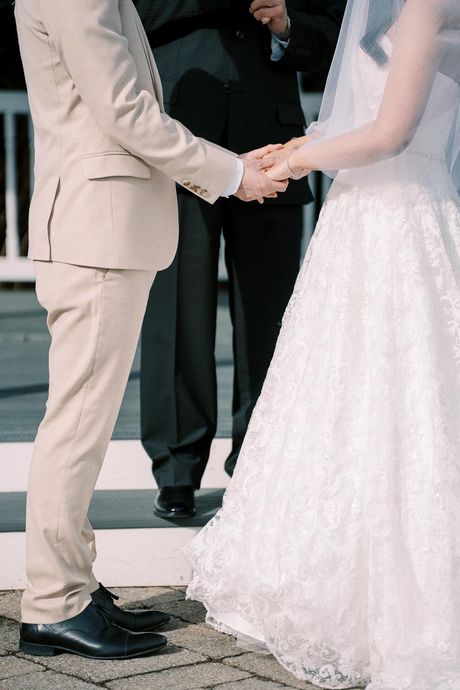 Bride and groom holding hands during outdoor wedding ceremony, wearing elegant attire.