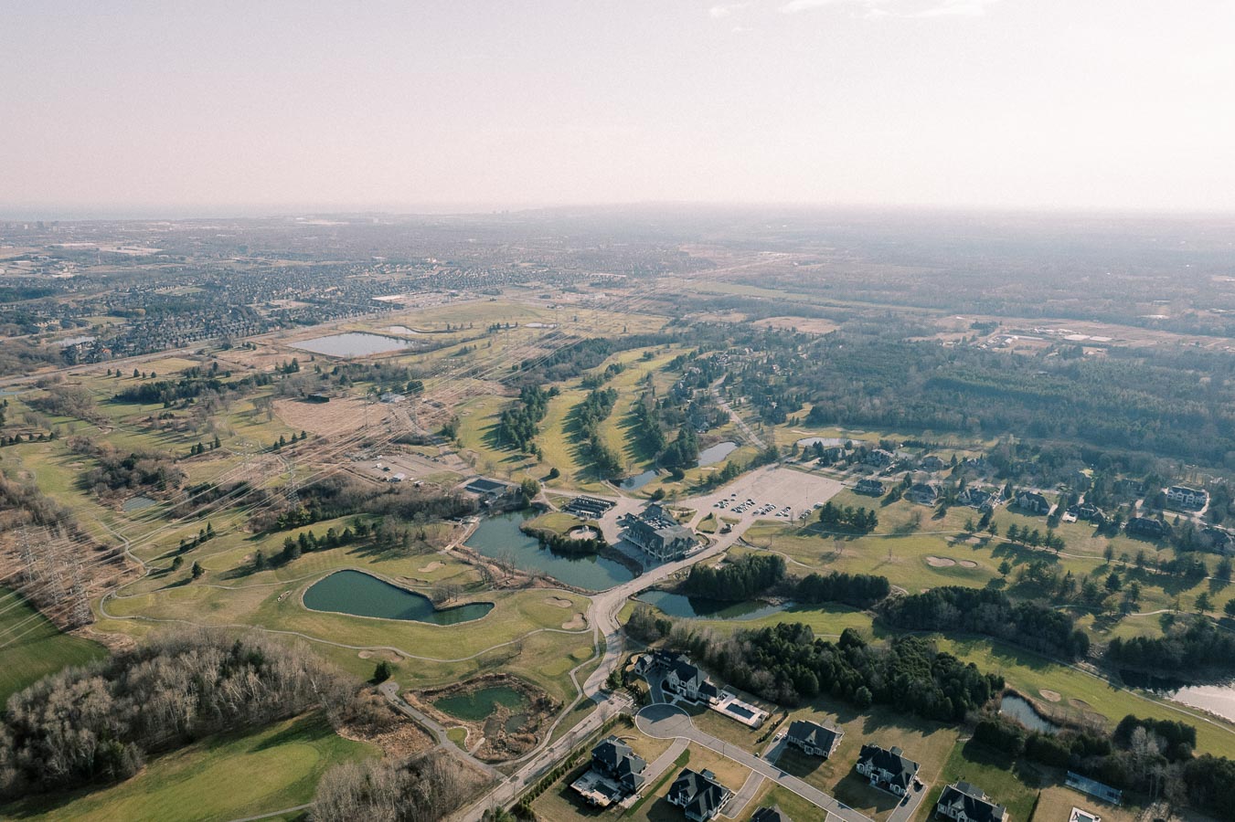 Aerial view of a sprawling golf course surrounded by lush greenery and residential areas, featuring winding pathways, serene water bodies, and a clear sky overhead. Ideal for nature lovers and golf enthusiasts.