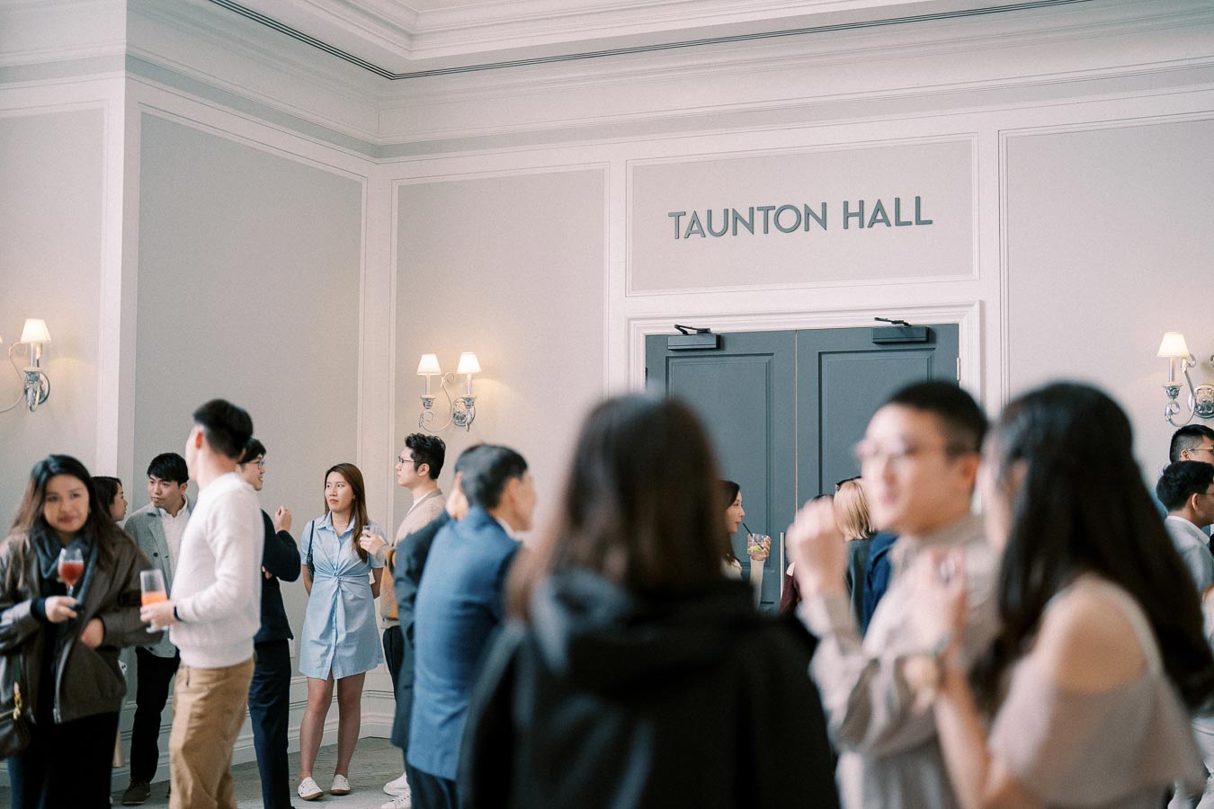 People networking at a social event in Taunton Hall, engaged in conversation and holding drinks, creating a vibrant and connected atmosphere.