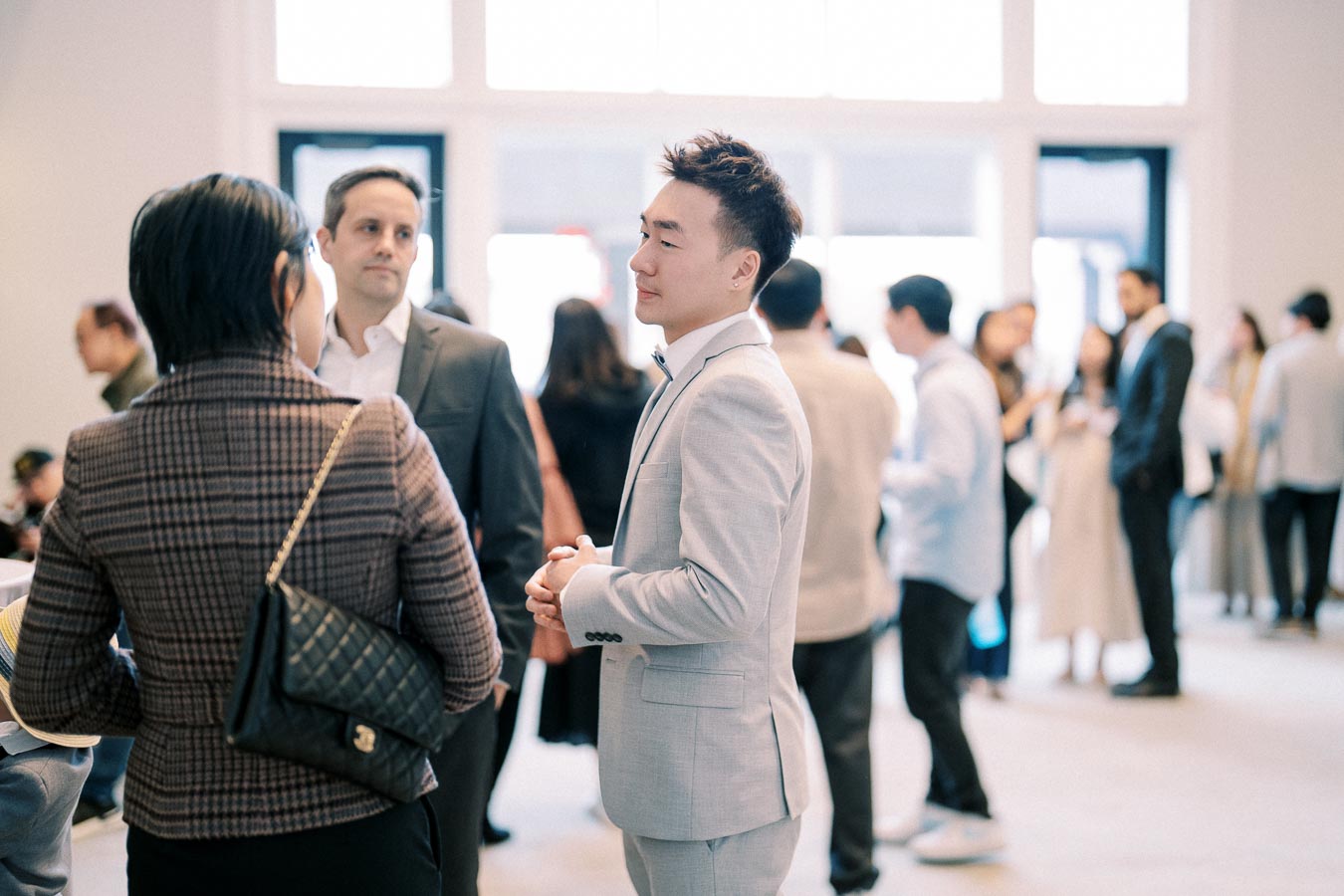 Group of professionals networking at a business event, with a focus on a man in a light gray suit engaging in conversation.