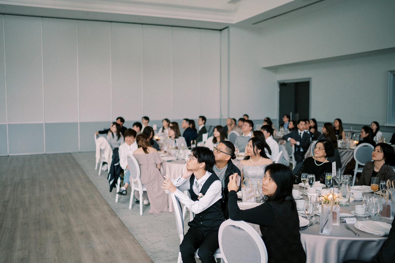 Audience attentively watching a presentation in a modern conference room, with elegantly set tables and guests dressed in formal attire.