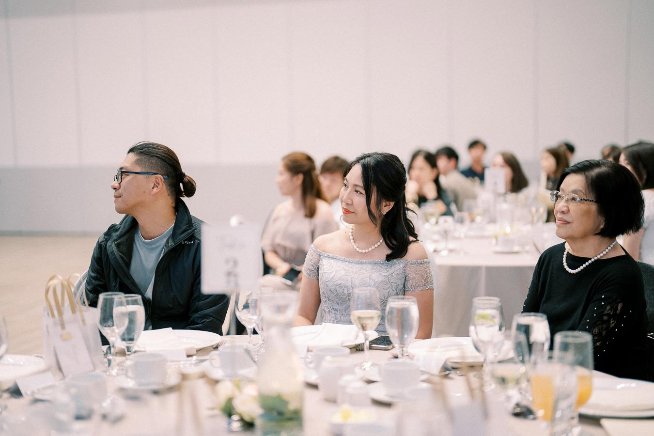 Group of elegantly dressed people sitting at a banquet table with glasses and plates during a formal event.
