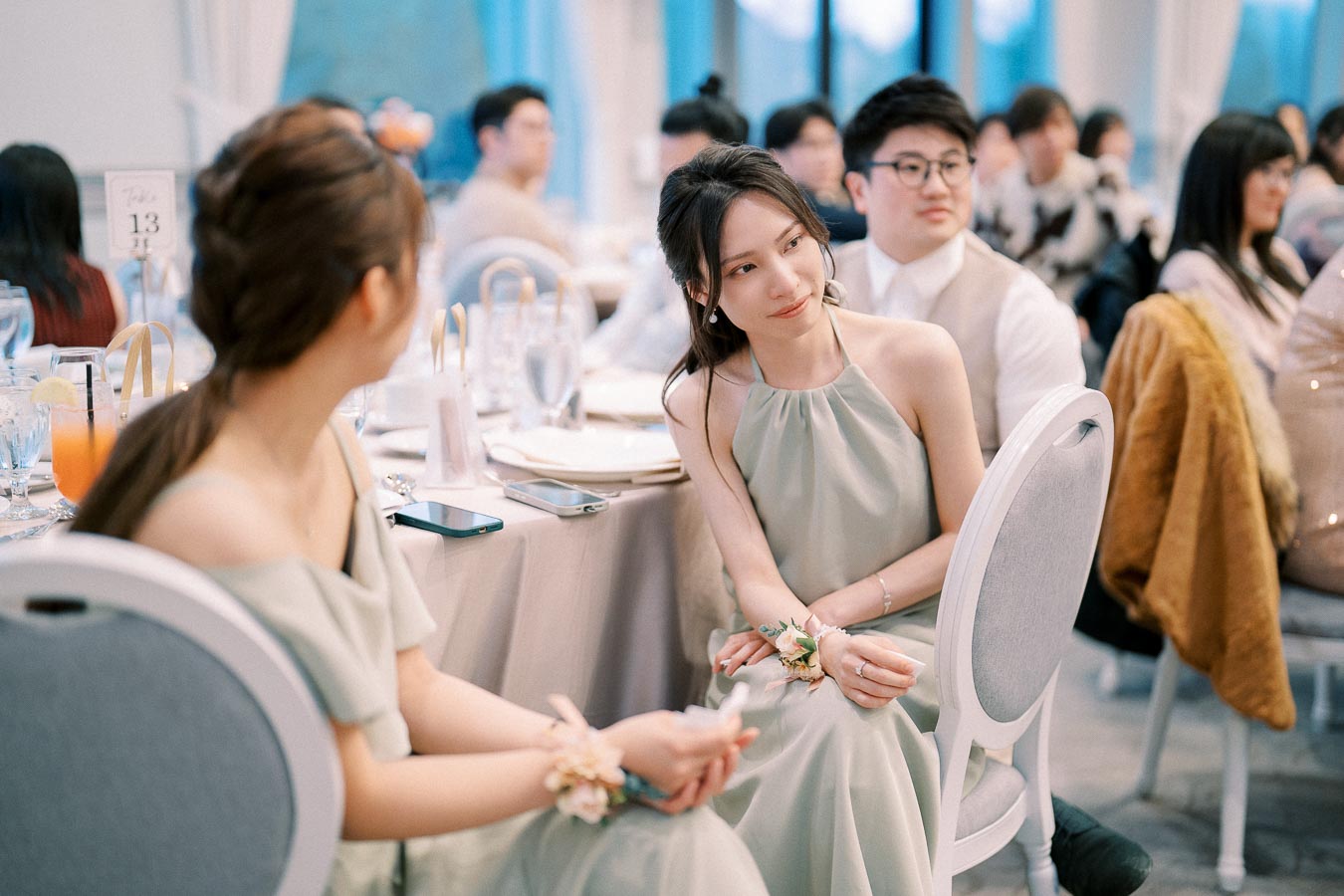 Guests seated at elegantly decorated tables, wearing formal attire, at a wedding reception, with natural lighting providing a serene ambiance.