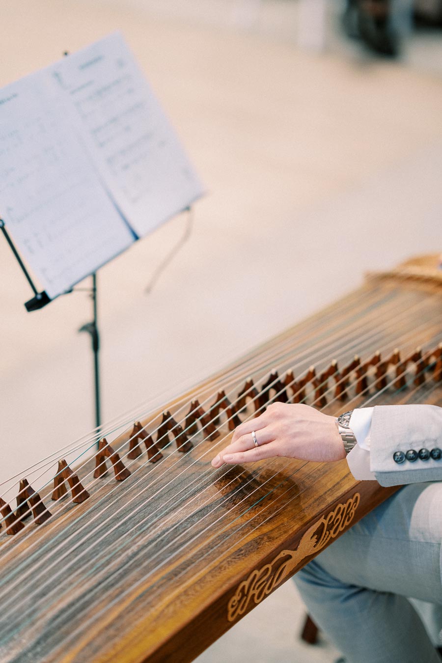 A person wearing a gray suit playing a traditional string instrument with sheet music in the background, emphasizing cultural music performance.