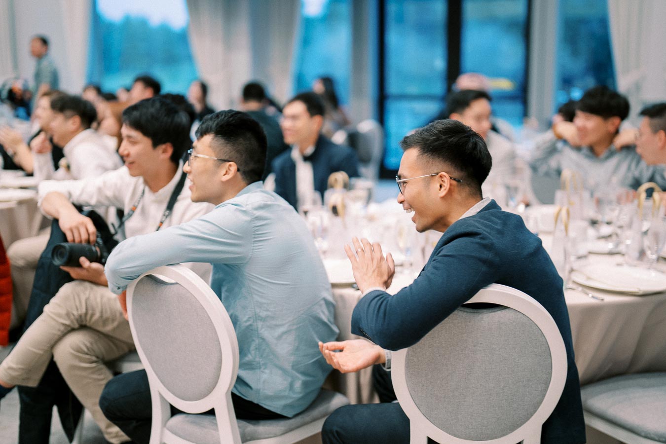 A group of people sitting at tables in a conference room, engaged in discussion and listening attentively, suggesting a professional networking event or seminar.