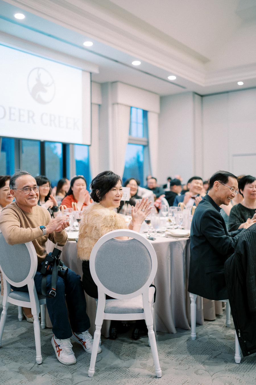 A group of people clapping at an elegantly set banquet table in a Deer Creek event venue.