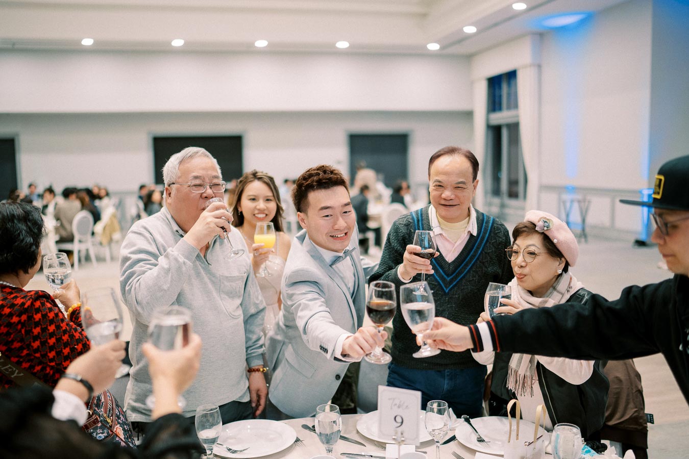 A group of people at a formal dining table raising glasses for a toast. The diverse group is smiling and celebrating at an indoor event, creating a festive and joyful atmosphere.