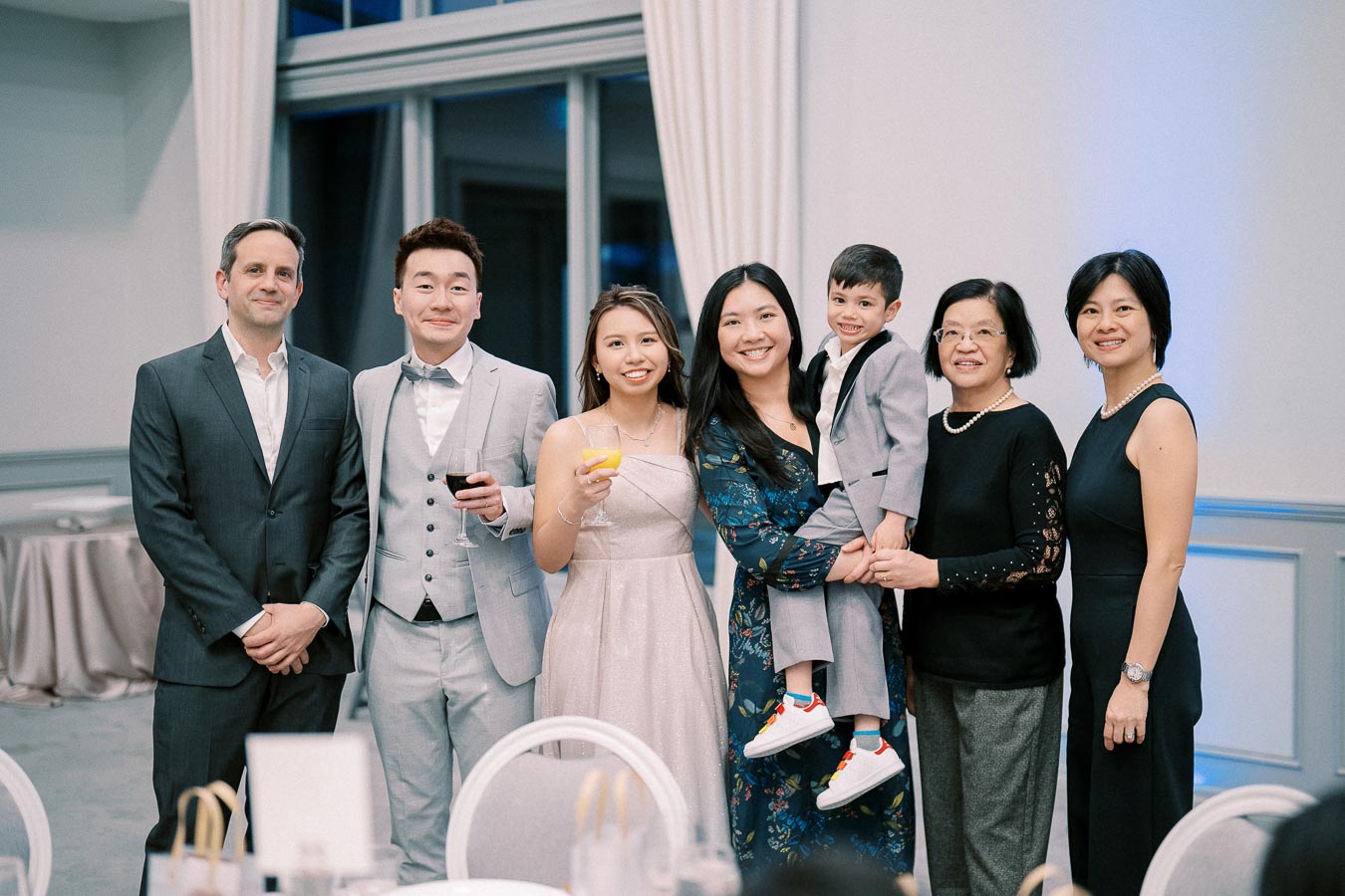 A group of seven people dressed in formal attire posing indoors at an event, displaying a celebratory atmosphere with smiles and holding drinks.