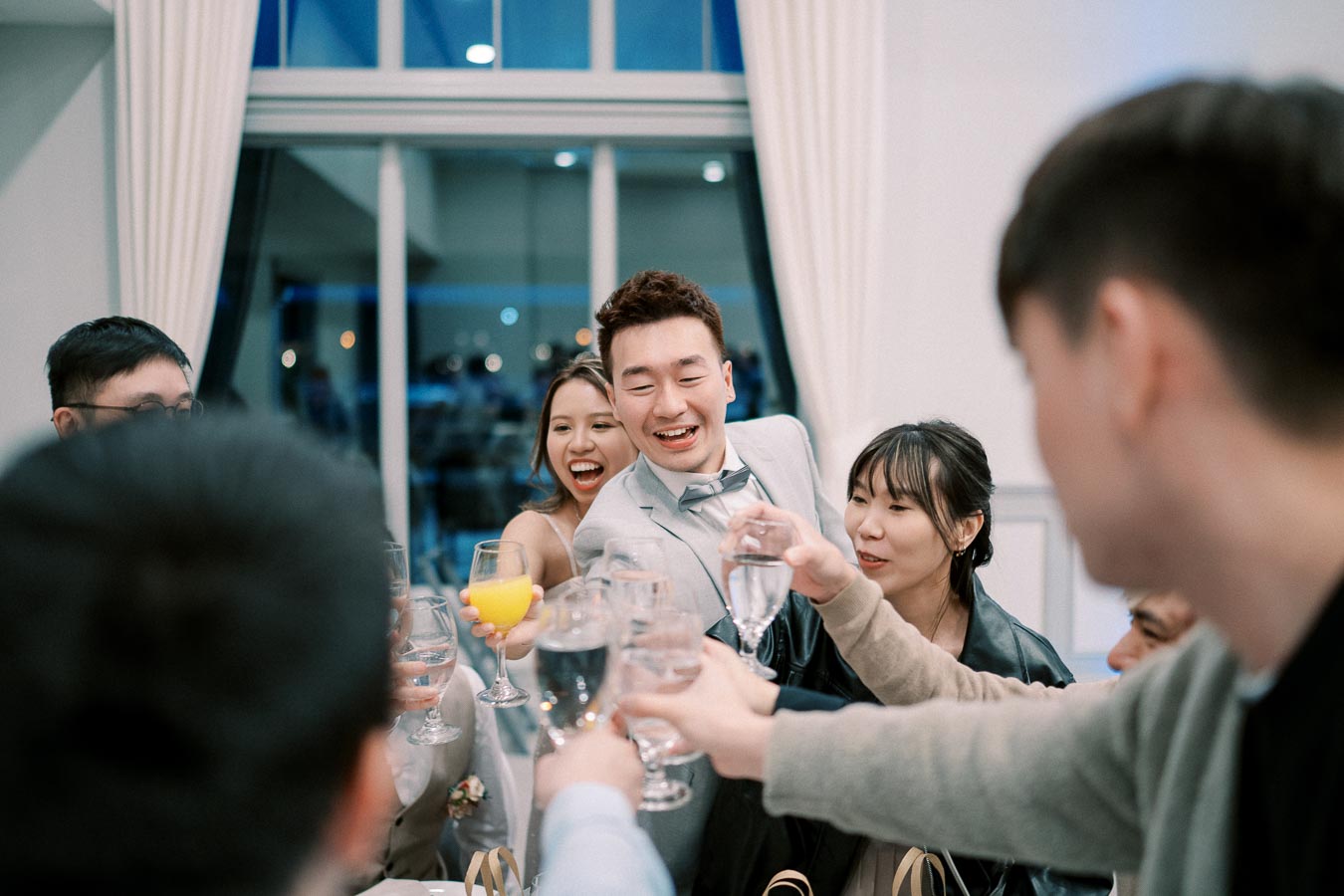 Group of friends joyfully toasting with glasses at a celebration inside a brightly lit room.