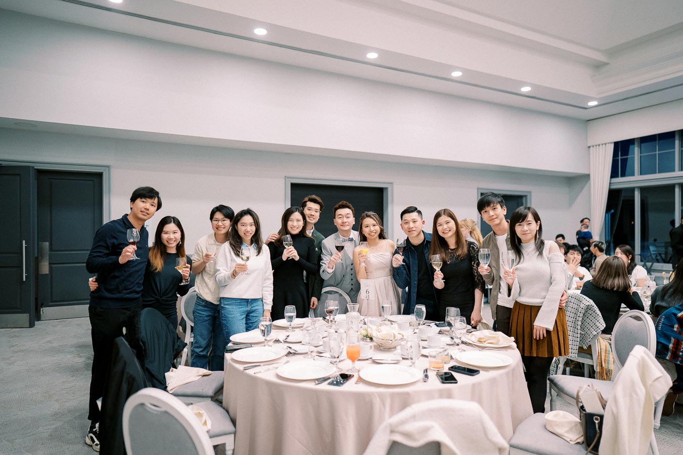 A group of people smiling and holding glasses while gathered around a beautifully set dinner table at an elegant indoor event.