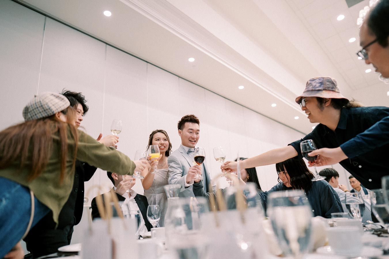 Group of people celebrating and toasting with wine glasses at a festive indoor event, surrounded by elegant table settings.