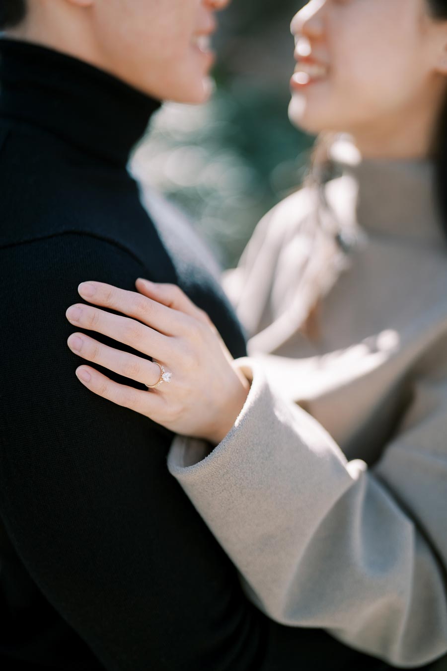 A close-up shot of a couple embracing, highlighting the woman's engagement ring as she rests her hand on the man's shoulder.