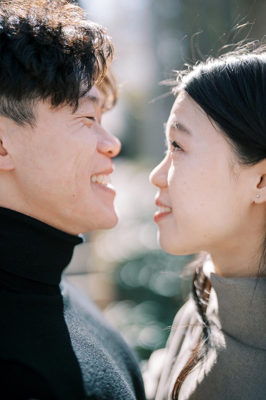 A couple smiling at each other in a close-up shot, capturing a moment of affection outdoors.