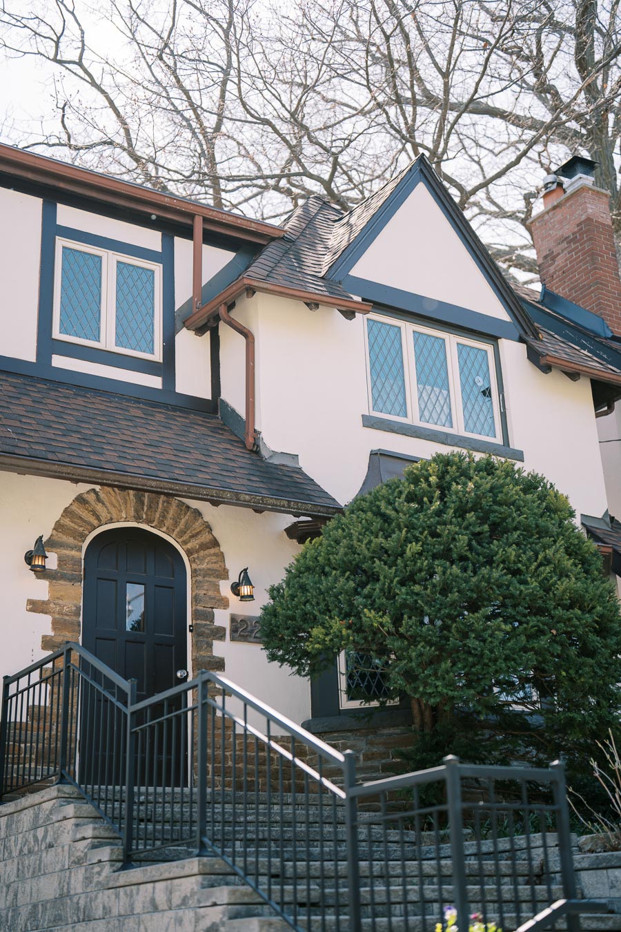 A charming Tudor-style house with a steep roof and decorative half-timbering, featuring a stone archway entrance and a brick chimney.