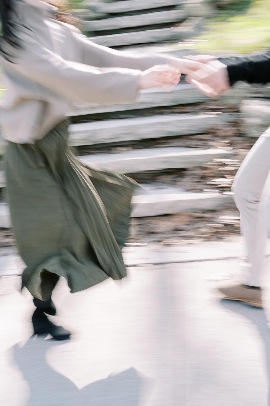A blurred photograph captures two people holding hands and spinning, creating a sense of motion and energy. The background features stone steps, suggesting an outdoor setting.
