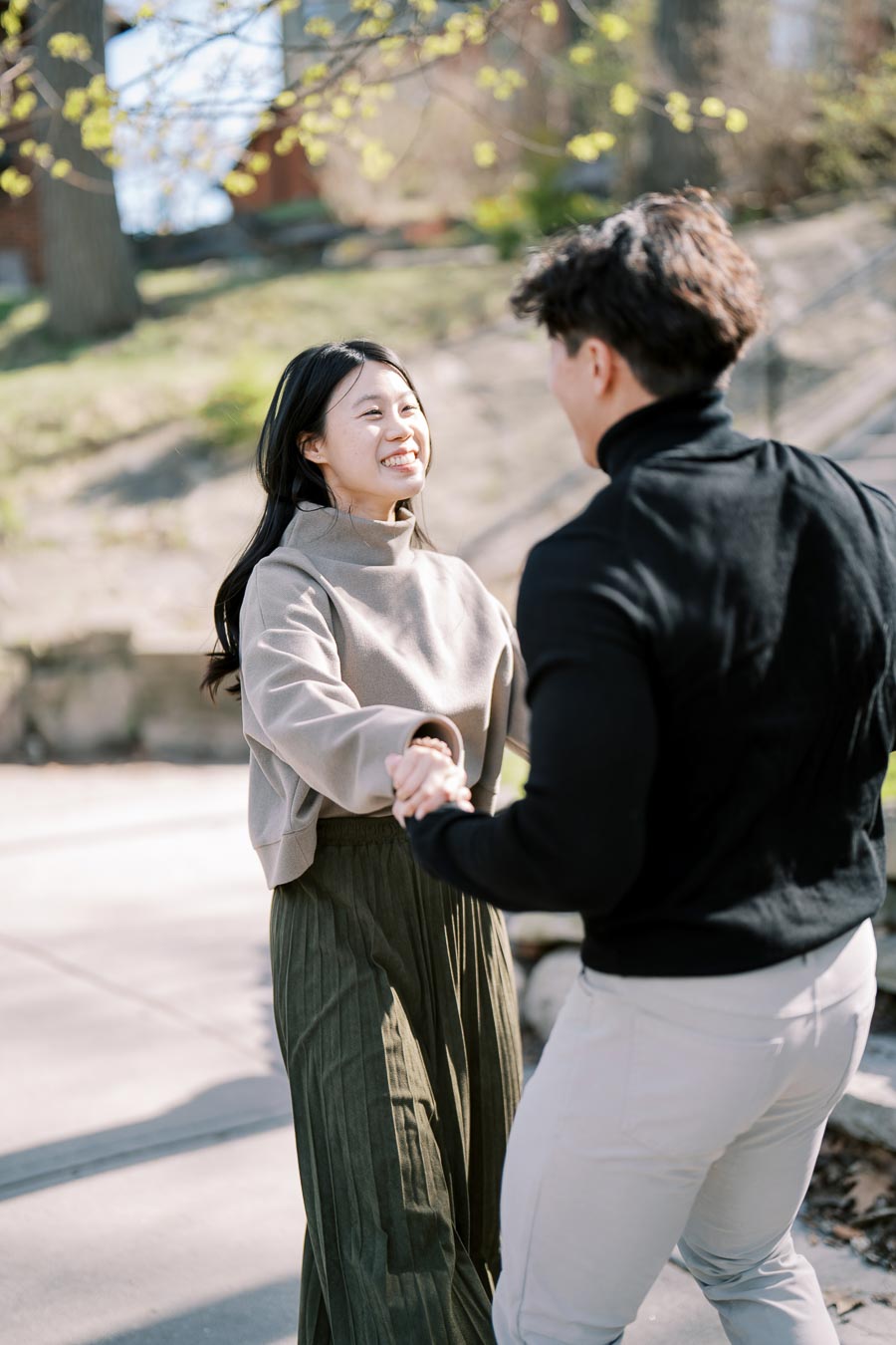 A couple enjoys a sunny day outdoors, holding hands and smiling at each other.