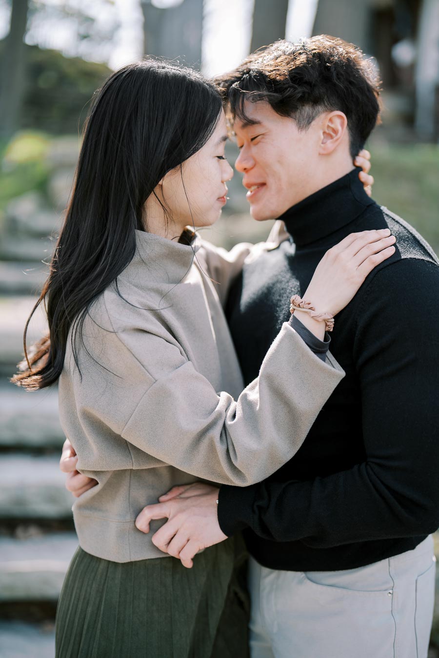 A couple shares an intimate moment outdoors, embracing each other with eyes closed.